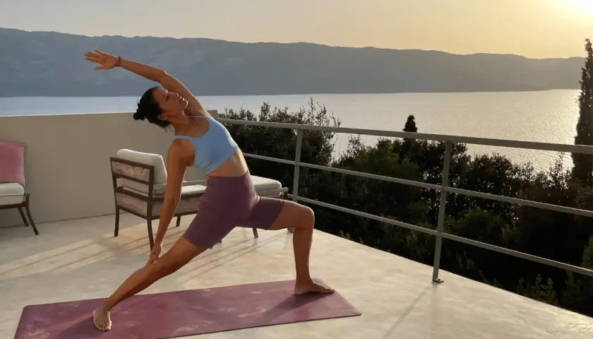 Mujer en postura de yoga en terraza con vista al mar al atardecer. Un momento de **slow life** y conexión.