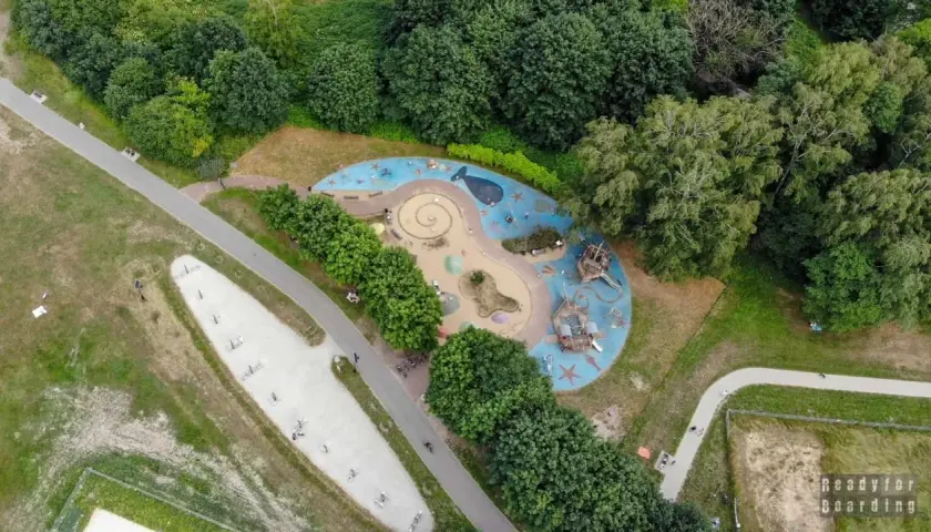 Kolorowy plac zabaw w kształcie fali z wielorybem i statkami pirackimi, otoczony zielenią. Idealne miejsce na zabawę dla dzieci w Łodzi.
