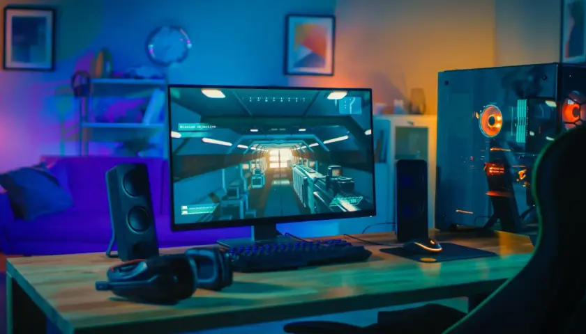 Bureau de jeu avec PC puissant, écran affichant un jeu vidéo, clavier, souris et casque. Ambiance lumineuse, parfait pour config windows 11.