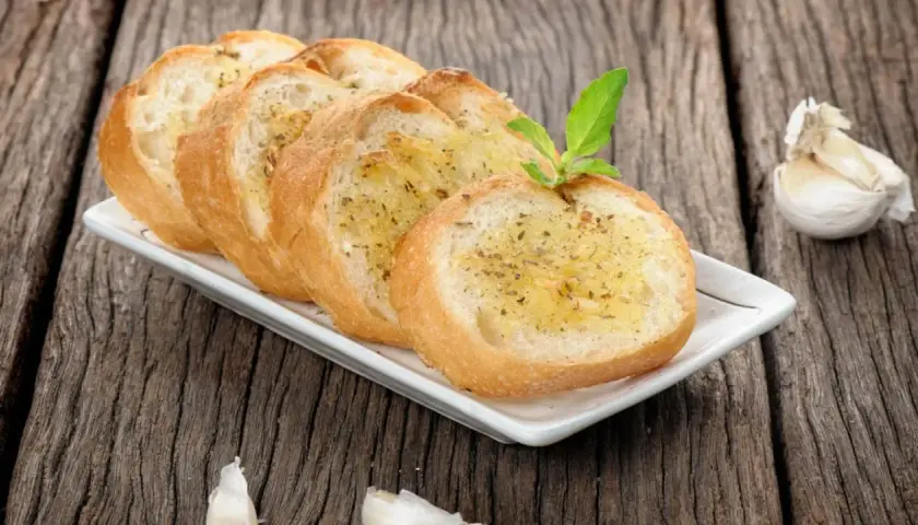 Tranches de pain grillé à l'ail, garnies d'herbes, rappelant la préfou recette traditionnelle. Une tête d'ail repose à côté.