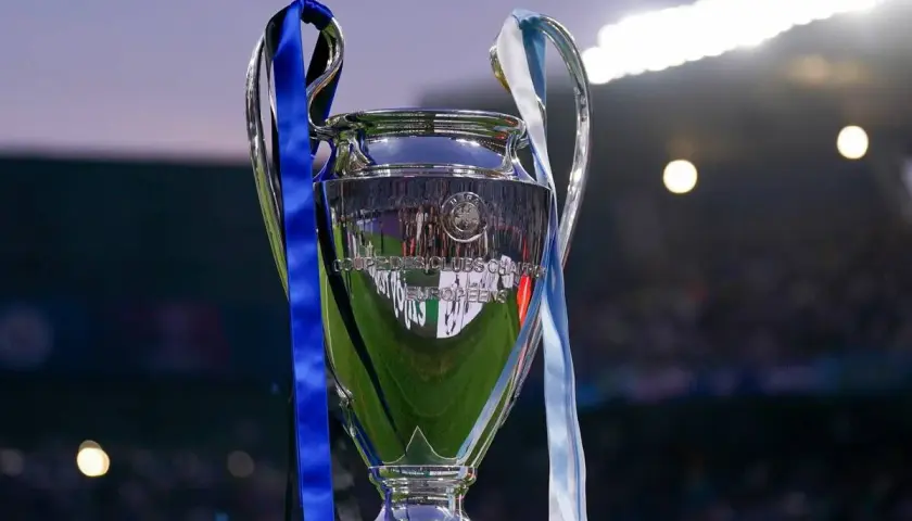 Trofeum Ligi Mistrzów, symbol marzeń i celów w piłkarskich rankingach. Błyszczący puchar z niebieskimi i jasnymi wstążkami, odbijający światła stadionu.
