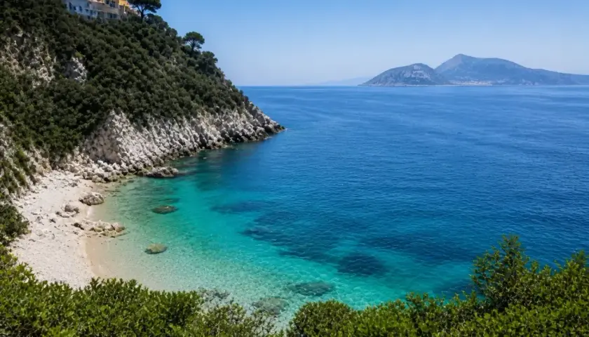 Vue d'une crique aux eaux turquoise cristallines, avec une colline verdoyante et des maisons blanches perchées, près d'une île à côté de Capri.
