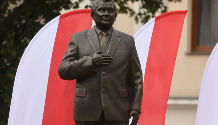 Pomnik Lecha Kaczyńskiego, jednego z wielu w Polsce, stoi na tle biało-czerwonych flag.