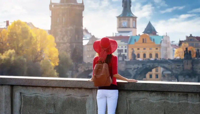 Kobieta w czerwonym kapeluszu podziwia praskie praga nietypowe atrakcje, w tym Most Karola i wieże.
