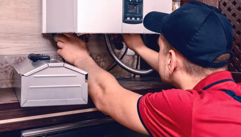 Instalator pracuje przy kotle gazowym, podłączając przewody. W tle widać metalową skrzynkę, która może być pomocna, gdy zastanawiamy się, jak zalać grzejnik elektryczny.