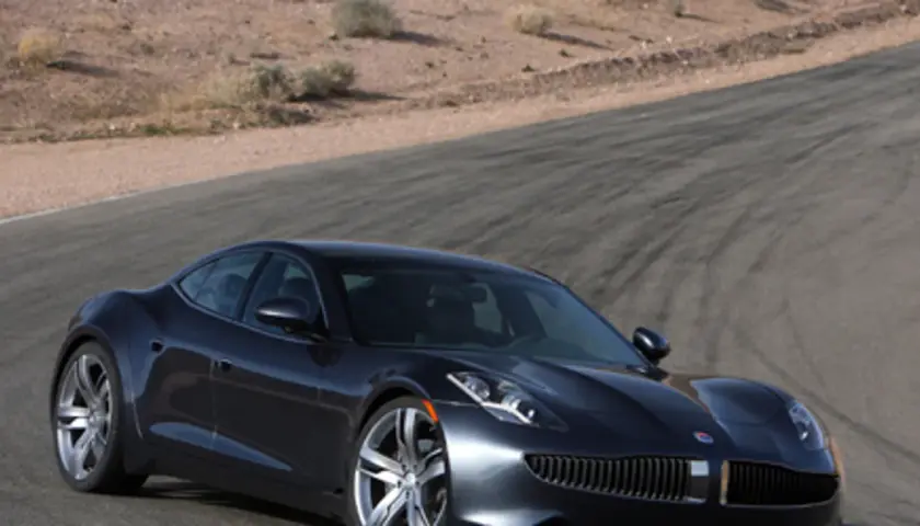 Elegancki, ciemnoszary Fisker Karma na torze wyścigowym, z pustynnym krajobrazem w tle.