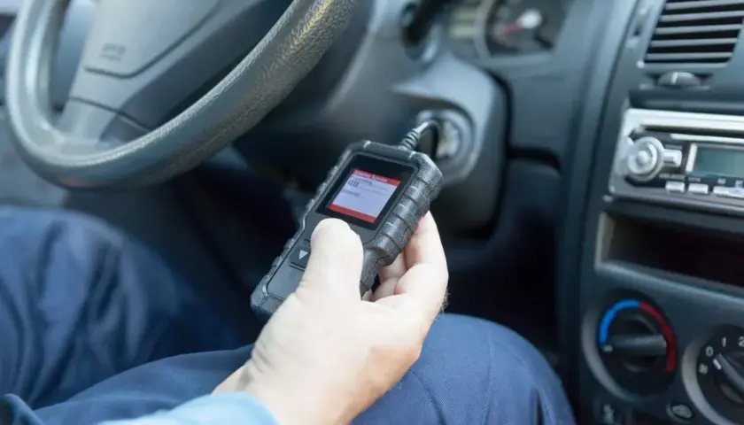 Ręka trzymająca skaner diagnostyczny OBD w samochodzie.