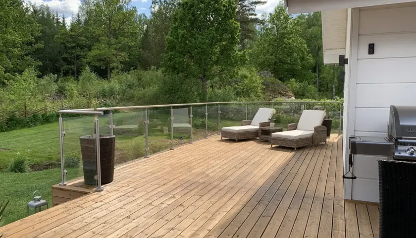 Nyligen oljad altan med solstolar och grill. Vacker utsikt över grönskande skog.