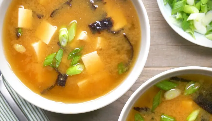 Two bowls of steaming nori soup, filled with tofu cubes and green onions, are ready to be enjoyed.