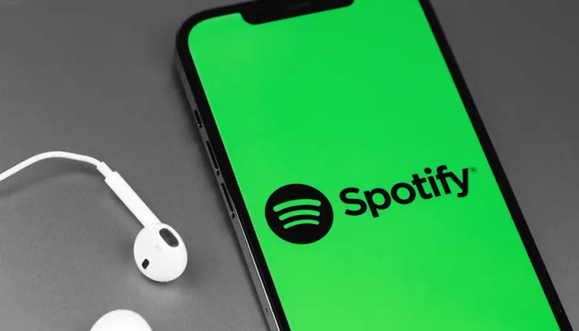 Telefon z zielonym ekranem i logo Spotify, obok białe słuchawki. Słuchaj muzyki za darmo dzięki Spotify free.