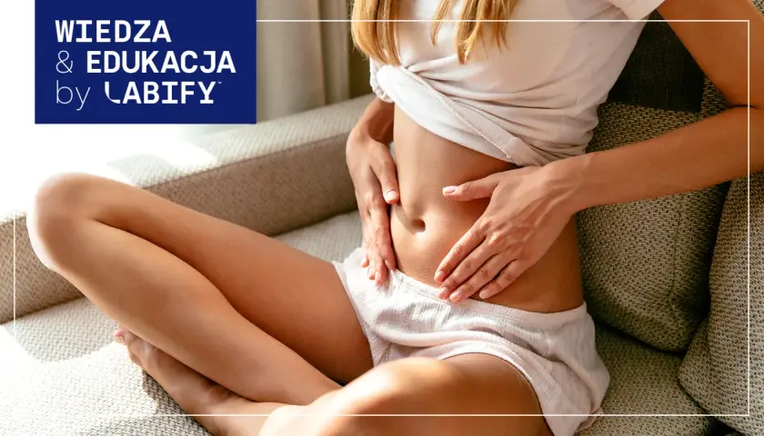 Kobieta trzyma się za brzuch, szukając ulgi co na gazy. Wiedza i edukacja by Labify.