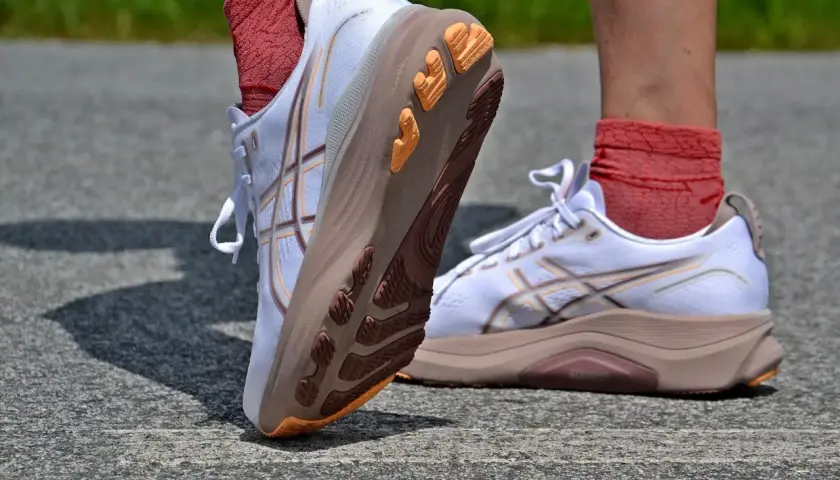 Białe buty do biegania Asics z pomarańczowymi akcentami na podeszwie. Firma Asics słynie z innowacyjnych rozwiązań.