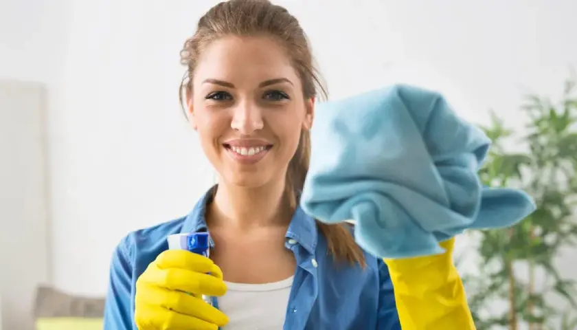 Donna sorridente con guanti gialli e panno blu, pronta a pulire le vetrate scorrevoli.