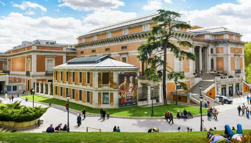 Muzeum Prado w Madrycie z ludźmi odpoczywającymi na trawie i zwiedzającymi.