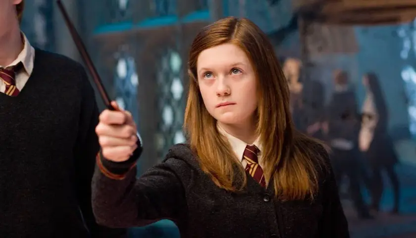 Bonnie Wright jako Ginny Weasley w filmach o Harrym Potterze, z różdżką w dłoni, gotowa do rzucenia zaklęcia.