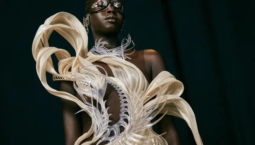 Mannequin portant une création avant-gardiste, un vêtement d'impression 3D aux formes organiques et futuristes, orné de détails argentés sur le visage.