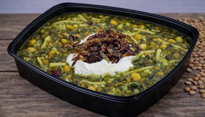 En skål med grön ash reshteh, en persisk örtsoppa med nudlar, kikärtor och linser, toppad med yoghurt och friterad lök.
