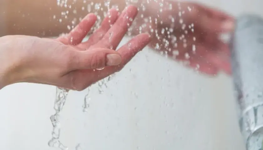 Manos bajo un chorro de agua fría, sintiendo el frescor al ducharse con agua fría.