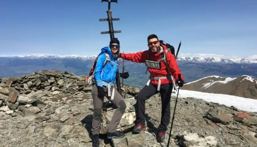 Dos montañistas celebran en la cima del Fontalba Puigmal, con un cruce metálico y vistas nevadas.
