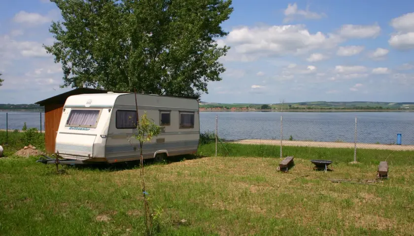 Przyczepa kempingowa na kempingu Merkur, nad jeziorem, pod drzewem.