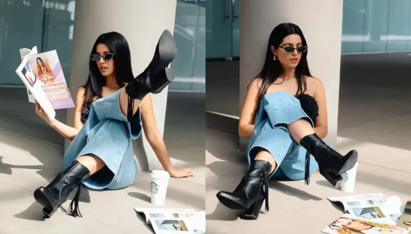Chica con gafas de sol y jeans anchos, luciendo unas **botas en verano** mientras lee una revista junto a un café.
