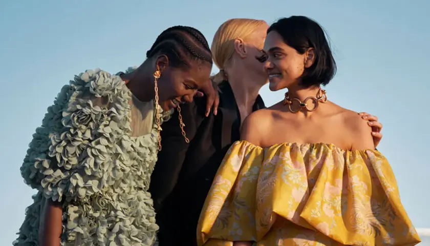 Tres mujeres ríen, una con un vestido verde con flores, otra con un collar dorado y un vestido amarillo estampado. Moda ecofriendly que es.