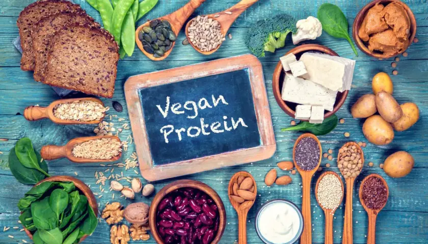 Na stole pełnym roślinnych produktów: chleb, fasola, orzechy, nasiona, tofu, warzywa i jogurt. To dowód, że wegańskie białko jest łatwo dostępne i smaczne.