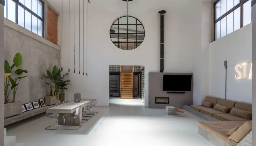 Großzügiges Loft mit Betonwänden, Stahlfenstern und einer Treppe. Der Stil ist **industrial chic**, mit Pflanzen und einer gemütlichen Sitzecke.