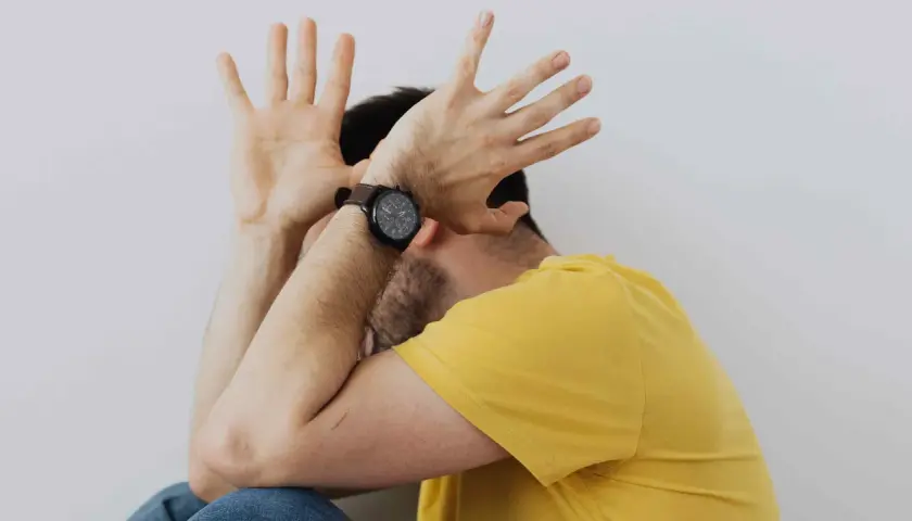 Uomo con le mani alzate a protezione del viso, forse per la paura delle cimici. Indossa una maglietta gialla e un orologio.