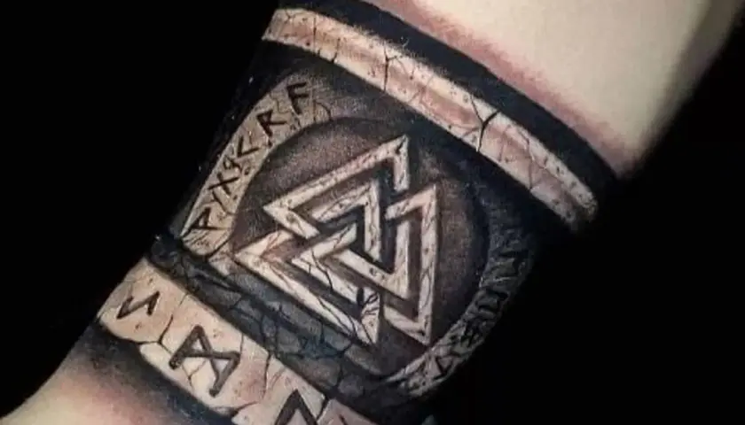 Tatuaż na przedramieniu z nordyckimi symbolami: Valhalla i runy. Wygląda jak starożytny artefakt.