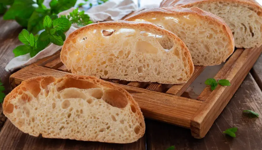Fette di pane soffice con alveolatura pronunciata, su un tagliere di legno, con foglie di menta fresca.