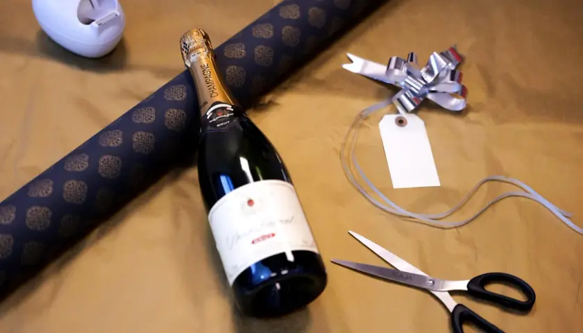 Vorbereitung, um mehrere Flaschen als Geschenk zu verpacken: Champagnerflasche, Geschenkpapier, Schere und Schleife liegen bereit.