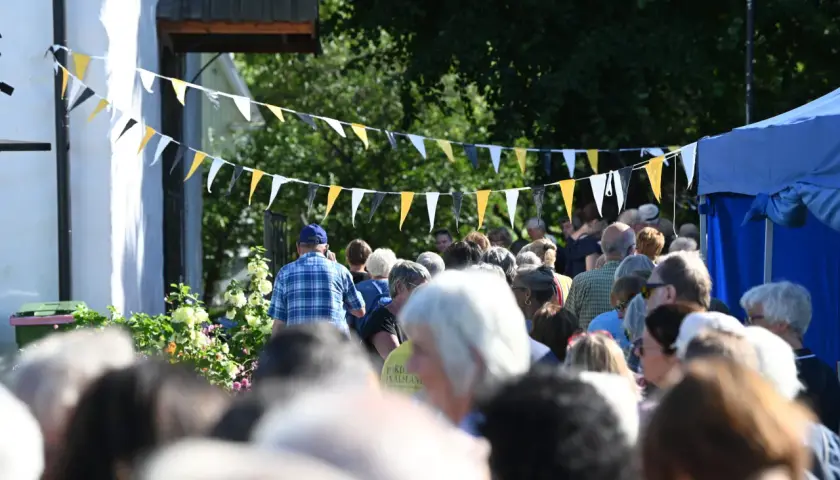 Folk samlas under flaggspel vid bokdagar i Dalsland. En man i rutig skjorta går framåt.