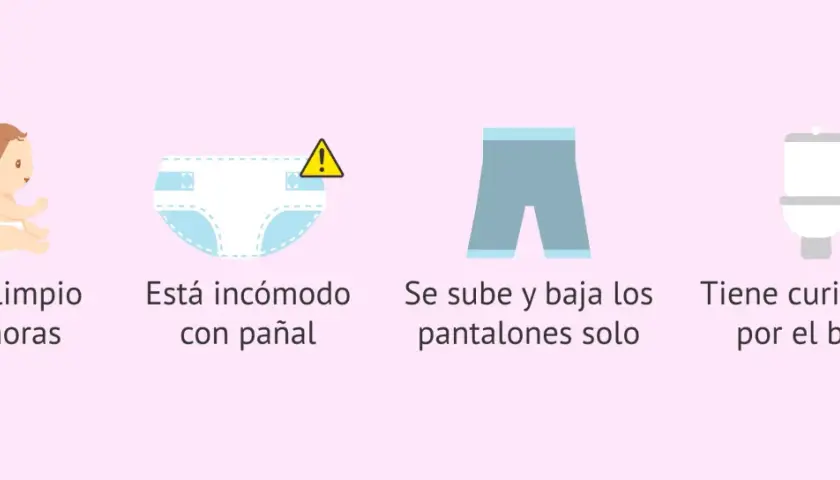 Bebé con pañal limpio, incómodo, bajándose pantalones y curioso por el baño. Señales para quitar el pañal.