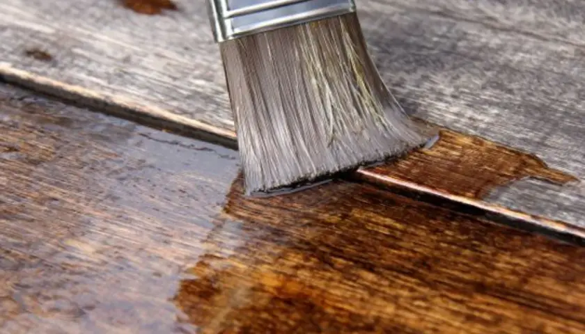 Pennello stende olio paglierino per legno su assi grezze, nutrendo e proteggendo la superficie.