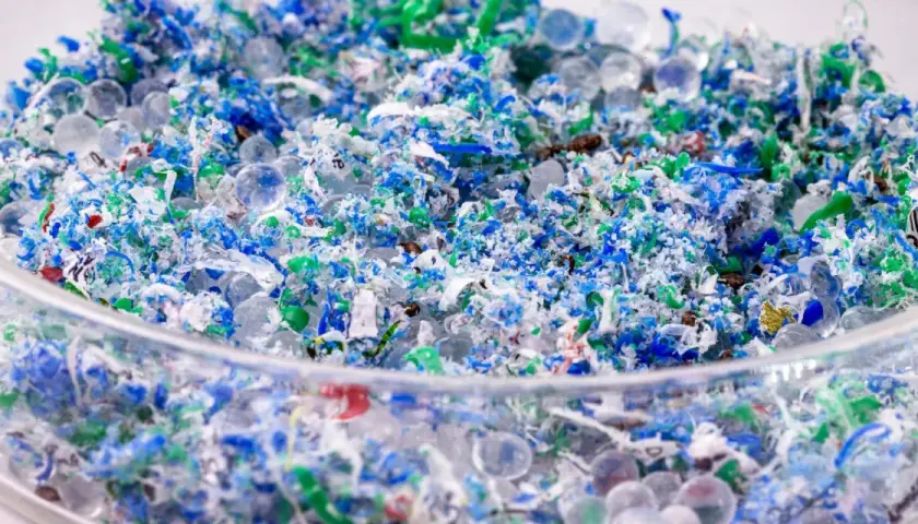 Kolorowe fragmenty plastiku i przezroczyste kuleczki, przypominające mikrokoraliki, tworzą obraz zanieczyszczenia. To mikroplastik w wodzie, widoczny w szklanym naczyniu.