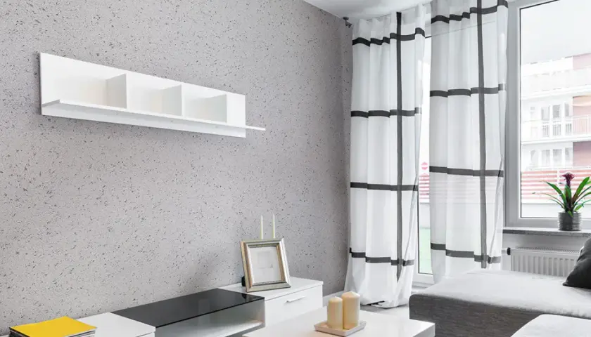 Nowoczesny salon z szarą ścianą pokrytą tynkiem japońskim o subtelnych wzorach. Białe meble i zasłony w kratę.