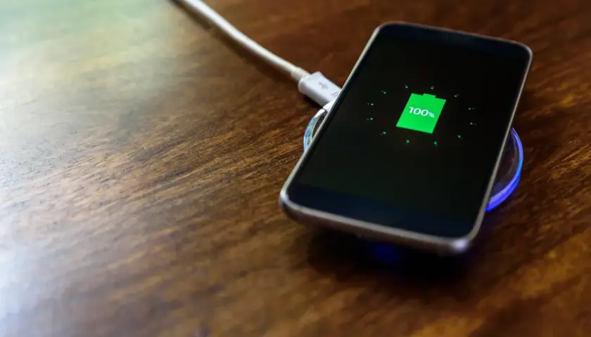 Telefon na ładowarce indukcyjnej osiągnął 100%. Warto ładować telefon do pełna, by zapewnić mu długą żywotność baterii.