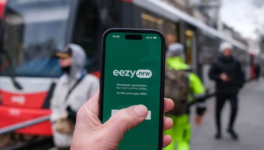 Hand hält Smartphone mit eezy.nrw App. Einfach einchecken, auschecken und nur nach Luftlinie zahlen in Westfalen.
