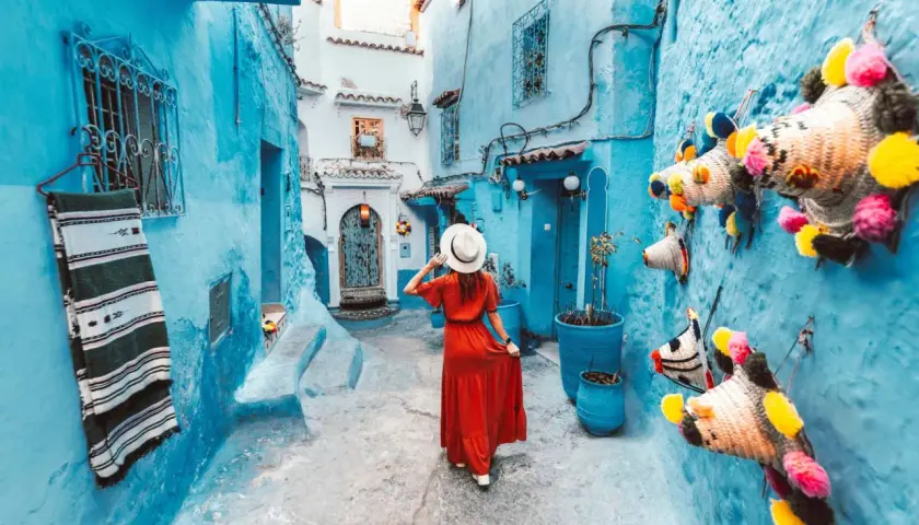 Una mujer con vestido rojo pasea por una calle de la **marruecos ciudad azul**, decorada con coloridas artesanías.