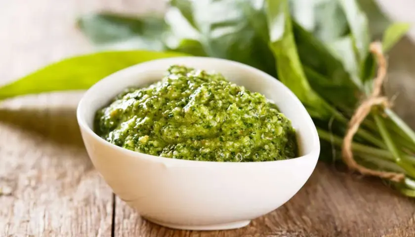 Pesto verde in una ciotola bianca, con un fascio di foglie di sedano fresche sullo sfondo. Perfetto per le tue ricette.