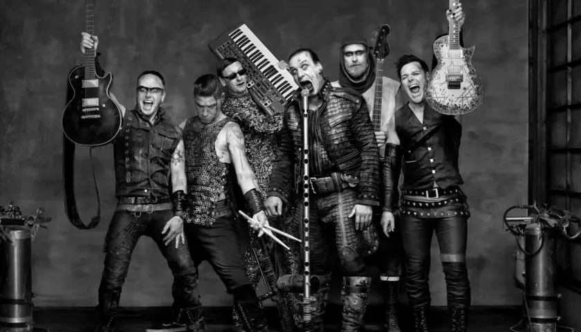 Zespół Rammstein, w tym Till Lindemann, gotowy do rockowego występu. W tle klawisze i gitary, jak w ich hicie "Radio".