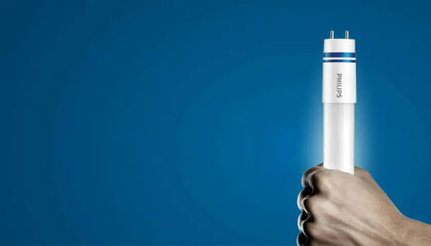 Dłoń trzyma nową żarówkę LED Philips, gotową do wymiany w tubie oświetleniowej.