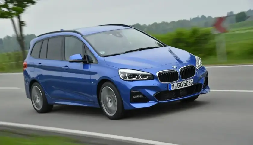 Niebieskie BMW 218i w wersji kombi pędzi po drodze, otoczone zielenią i drzewami.