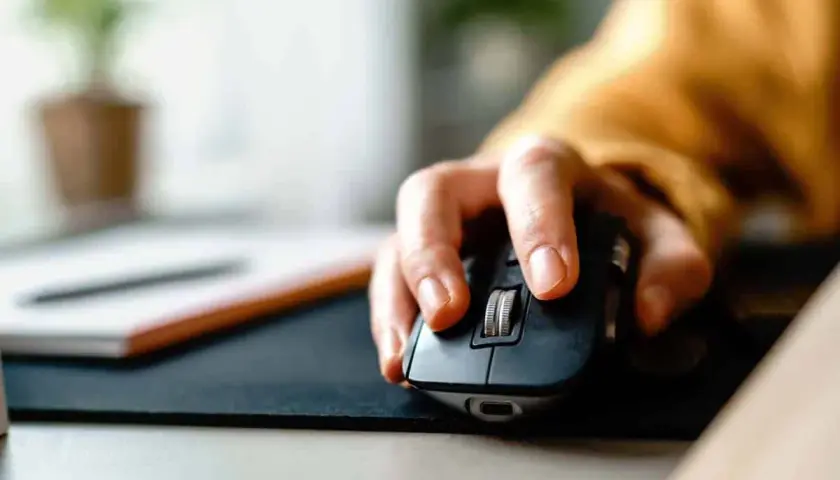 Eine Hand bedient eine Computermaus, die **Maus klickt doppelt**. Im Hintergrund ist eine Pflanze zu sehen.