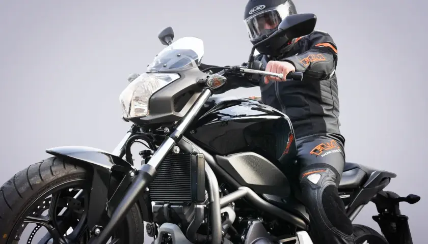 Motocykl od ilu lat? Młody motocyklista w czarnym kombinezonie i kasku na czarnym motocyklu.
