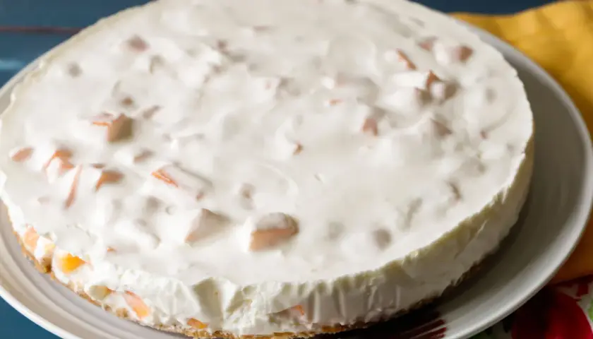 Torta fredda con una soffice crema al melone e pezzetti di frutta arancione.