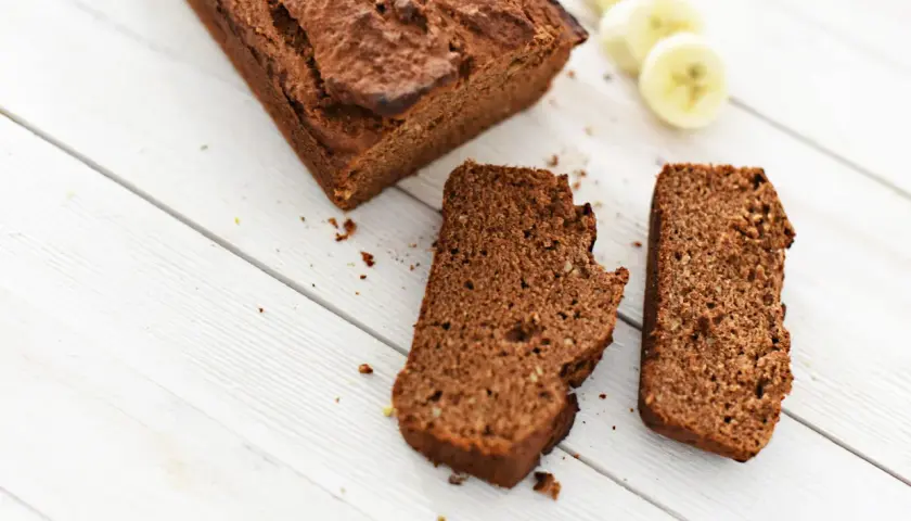 Chlebek bananowy Ani gotuje się na białych deskach. Obok leżą dwa kawałki ciasta i plasterki banana.