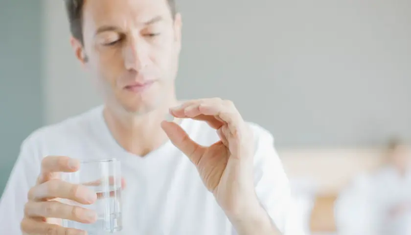 Mann hält Tablette und Glas Wasser, fragt sich, wie viel Magnesium bei Tinnitus hilft.