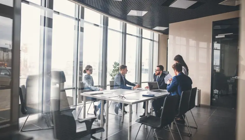 Des employés en tenue pour réunion travail discutent autour d'une table dans une salle de conférence lumineuse avec vue sur la ville.